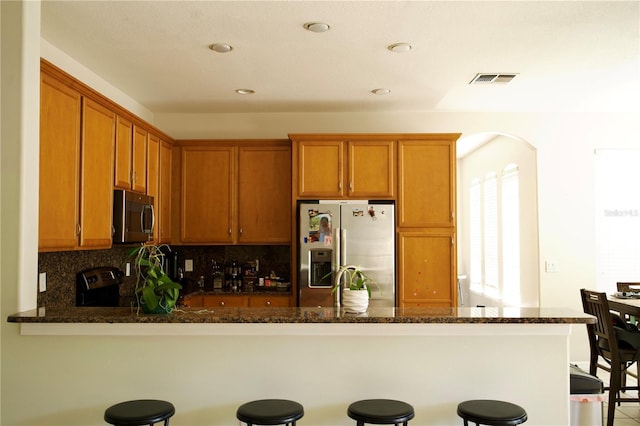 13520 Meadow Bay Loop, Orlando, FL 32824 - kitchen with a peninsula, dark stone counters, tasteful backsplash, appliances with stainless steel finishes, and a breakfast bar area