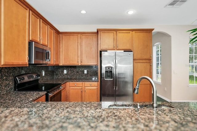13520 Meadow Bay Loop, Orlando, FL 32824 - kitchen featuring stainless steel appliances, dark stone counters, tasteful backsplash, arched walkways, and recessed lighting