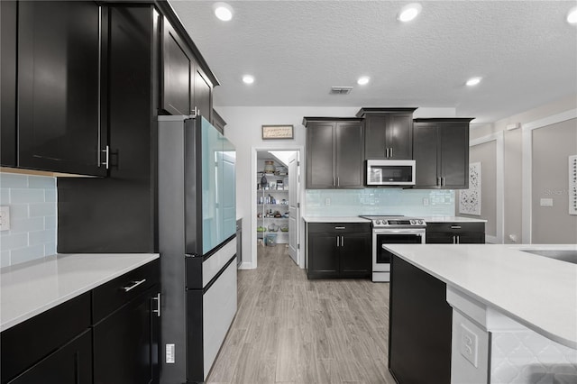 12048 Imaginary Way, Orlando, FL 32832 - kitchen featuring tasteful backsplash, stainless steel appliances, light wood finished floors, light countertops, and dark cabinets