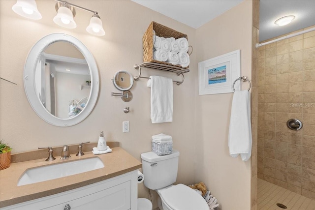 bathroom with a tile shower, toilet, and vanity