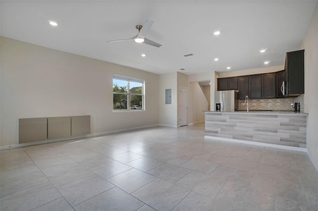 unfurnished living room with a sink, baseboards, ceiling fan, and electric panel