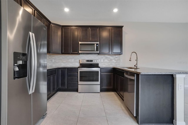 kitchen with a sink, a peninsula, light stone countertops, dark brown cabinets, and appliances with stainless steel finishes