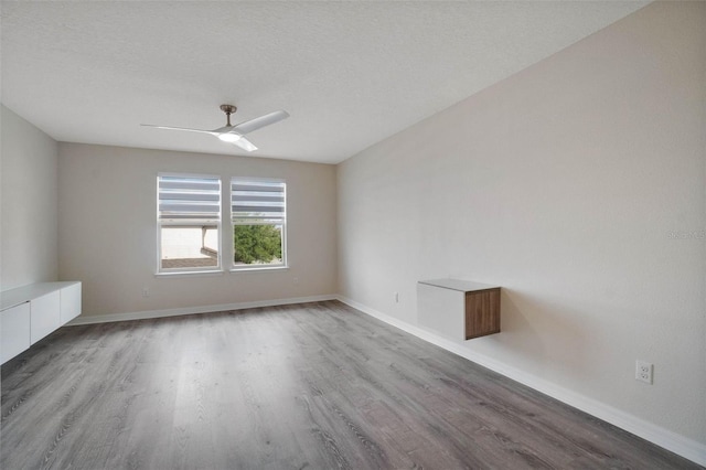 spare room featuring a textured ceiling, baseboards, wood finished floors, and a ceiling fan