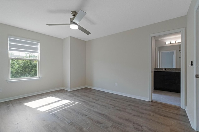unfurnished bedroom with a sink, ensuite bath, baseboards, and wood finished floors
