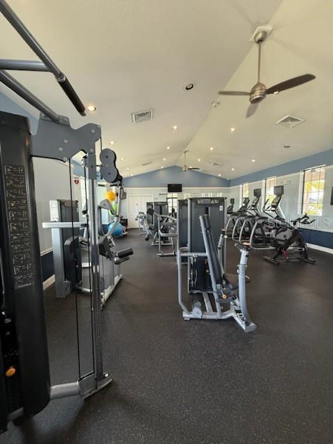 gym featuring a ceiling fan, baseboards, vaulted ceiling, and visible vents