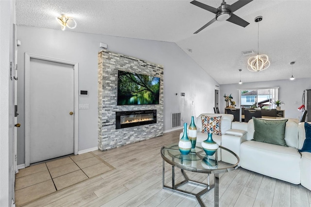 living room featuring a glass covered fireplace, a ceiling fan, visible vents, wood finished floors, and lofted ceiling