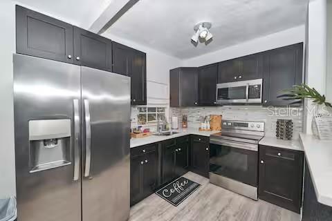 1405 Smith Dr N, Titusville, FL 32780 - kitchen featuring light countertops, dark cabinetry, stainless steel appliances, decorative backsplash, and a sink