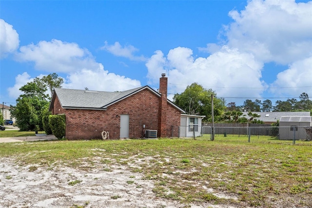 view of side of property featuring fence, a chimney, central AC, brick siding, and a lawn