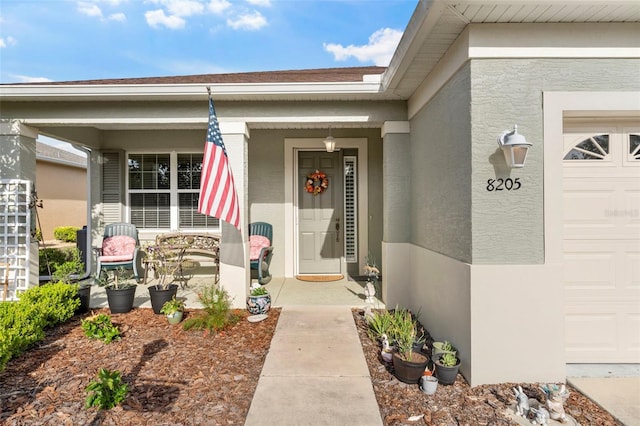 entrance to property with stucco siding, covered porch, and a garage