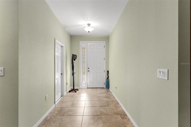 hallway with light tile patterned floors, baseboards, and a textured ceiling