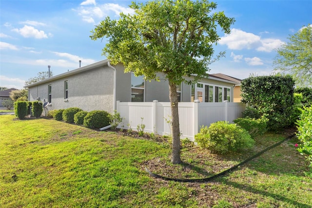 view of property exterior with a lawn, stucco siding, and fence