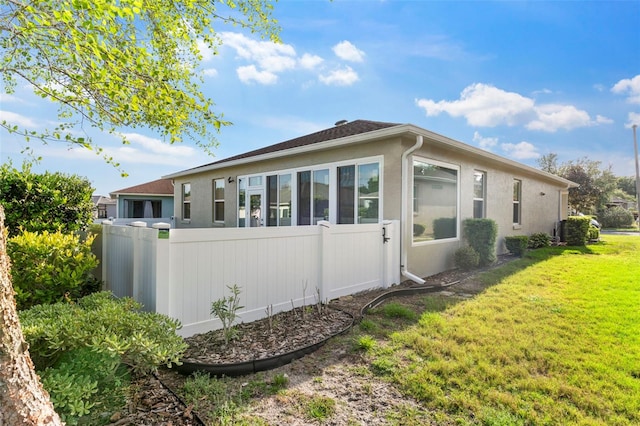 back of house with a lawn, stucco siding, and fence