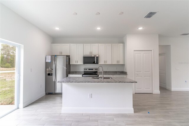 kitchen with an island with sink, light stone countertops, visible vents, stainless steel appliances, and a sink