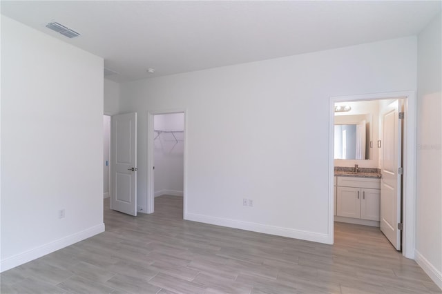 unfurnished bedroom featuring light wood-style flooring, baseboards, a spacious closet, and visible vents
