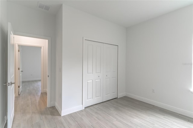 unfurnished bedroom featuring visible vents, baseboards, light wood-type flooring, and a closet