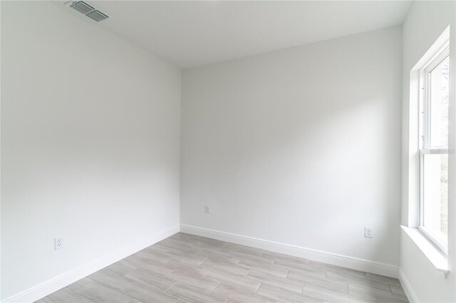 spare room featuring visible vents, light wood-style flooring, baseboards, and a healthy amount of sunlight