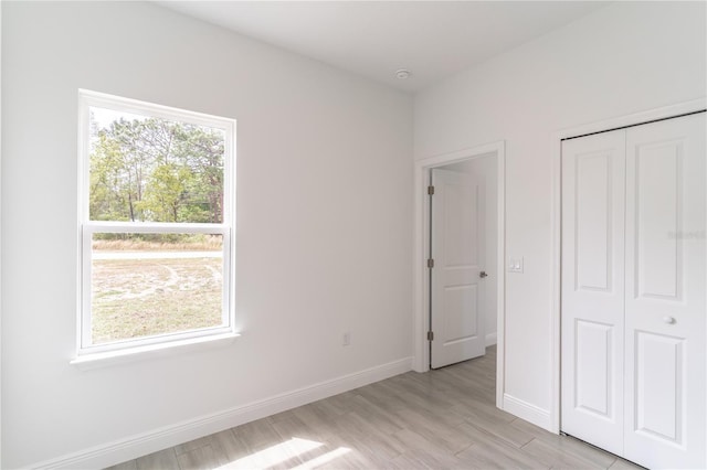 unfurnished bedroom with light wood-style floors, a closet, baseboards, and multiple windows