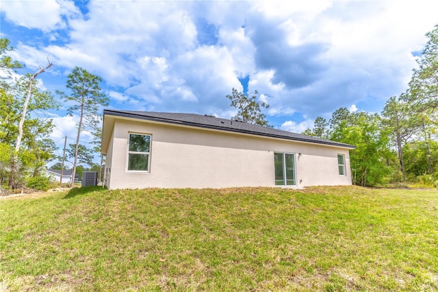 back of house featuring central AC unit, a lawn, and stucco siding