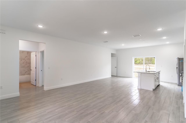 unfurnished living room featuring light wood-type flooring, a sink, and recessed lighting