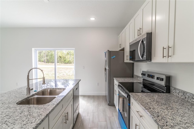 kitchen featuring light stone counters, a sink, white cabinetry, and stainless steel appliances