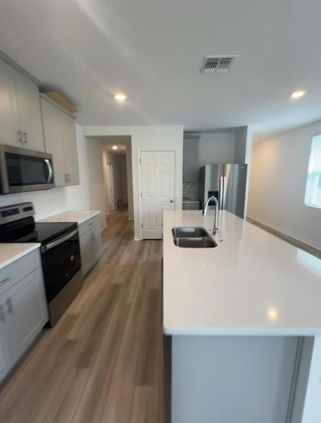 6028 Bimini Ave, Haines City, FL 33844 - kitchen featuring stainless steel appliances, a sink, gray cabinets, light countertops, and a center island with sink