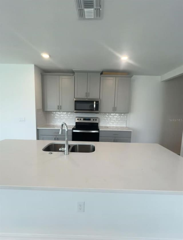 6028 Bimini Ave, Haines City, FL 33844 - kitchen featuring electric range, stainless steel microwave, gray cabinetry, backsplash, and a sink