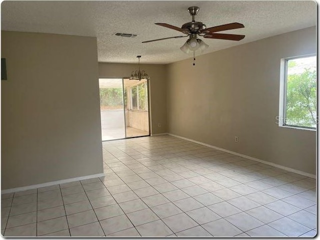 unfurnished room with a textured ceiling, visible vents, baseboards, and ceiling fan with notable chandelier