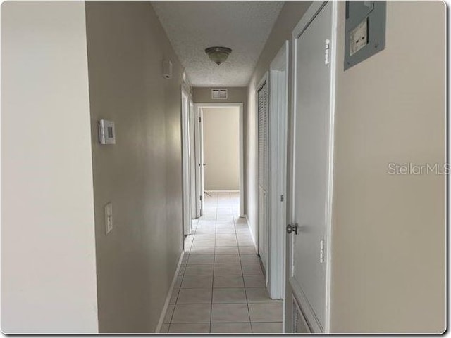 corridor featuring baseboards, light tile patterned flooring, a textured ceiling, and visible vents
