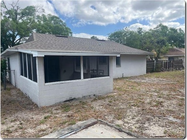 view of side of property with concrete block siding, fence, a shingled roof, and a sunroom