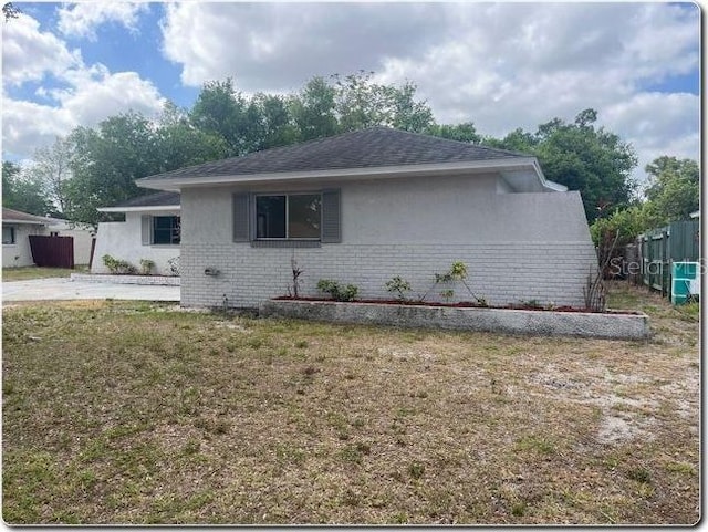 view of property exterior featuring a lawn, brick siding, fence, and stucco siding