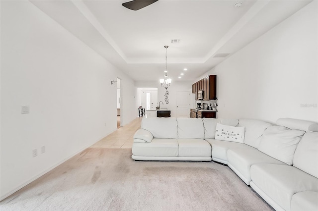 living room featuring visible vents, a raised ceiling, ceiling fan with notable chandelier, light colored carpet, and light tile patterned flooring