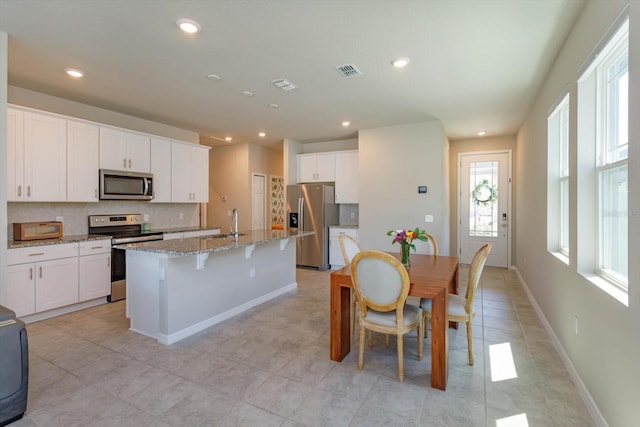 kitchen featuring visible vents, appliances with stainless steel finishes, a kitchen island with sink, a sink, and backsplash