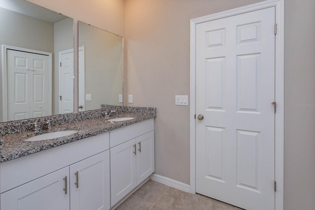 full bath with tile patterned floors, double vanity, baseboards, and a sink