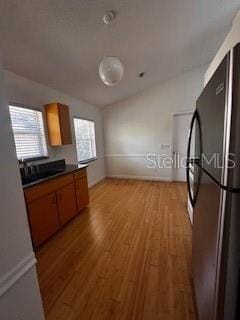 kitchen with brown cabinets, light wood-type flooring, freestanding refrigerator, and dark countertops