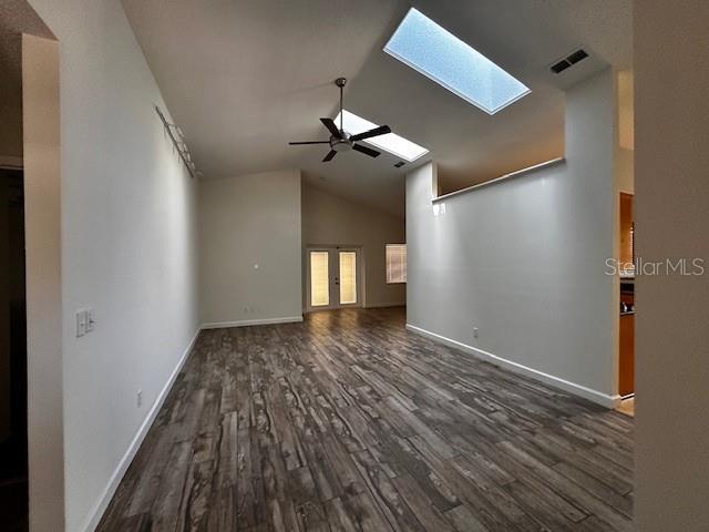 unfurnished living room featuring visible vents, a ceiling fan, dark wood-style floors, a skylight, and high vaulted ceiling