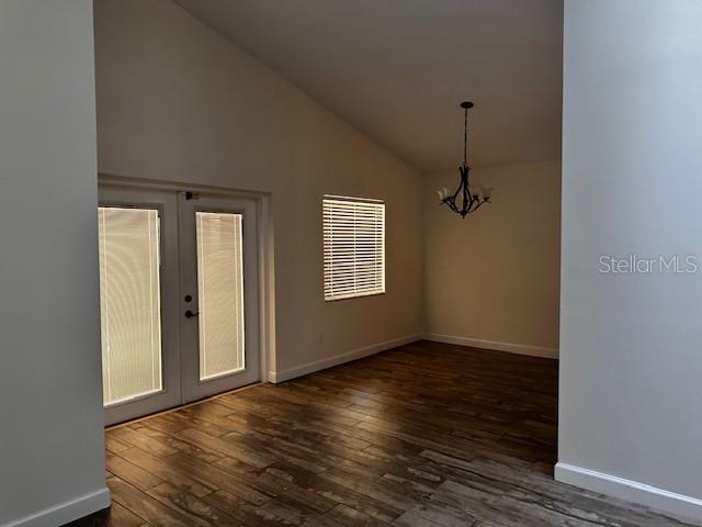 spare room featuring dark wood finished floors, vaulted ceiling, french doors, baseboards, and a notable chandelier