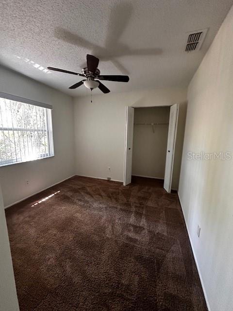 unfurnished bedroom featuring a textured ceiling, a closet, a ceiling fan, visible vents, and carpet flooring