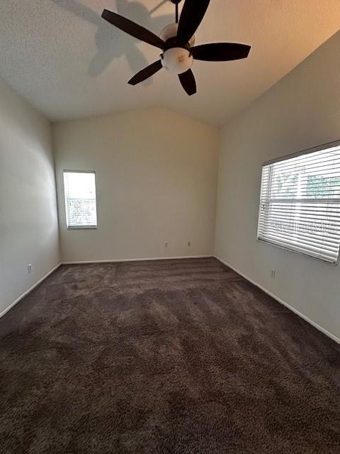 empty room featuring dark carpet, ceiling fan, vaulted ceiling, and baseboards