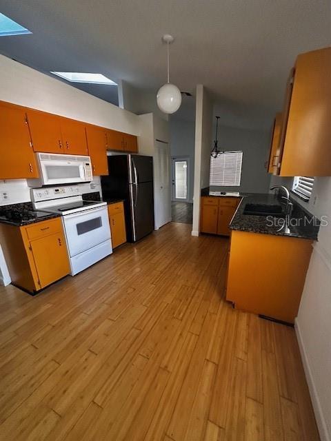 kitchen with a skylight, a sink, white appliances, and dark countertops