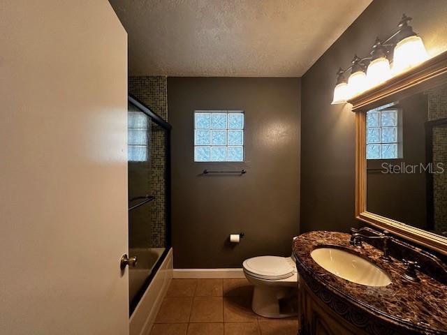 full bath with a textured ceiling, vanity, toilet, tile patterned floors, and baseboards