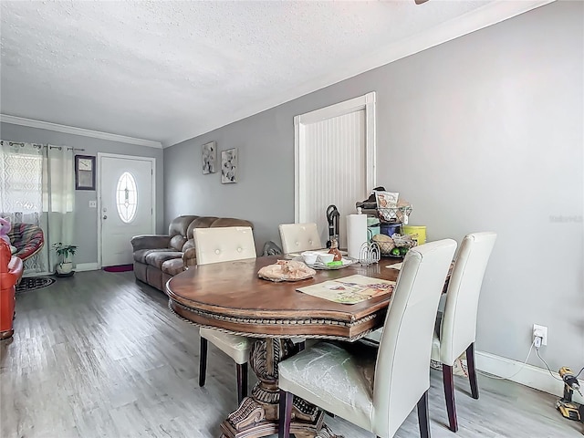 dining room featuring wood finished floors, ornamental molding, baseboards, and a textured ceiling
