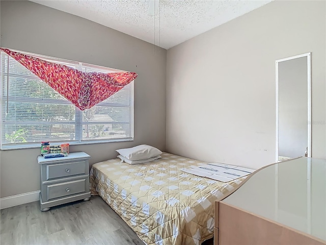 bedroom with light wood finished floors, baseboards, and a textured ceiling