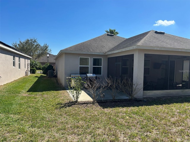 back of property with a sunroom, central air condition unit, stucco siding, a lawn, and roof with shingles