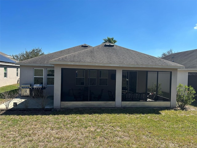 back of house featuring a sunroom, roof with shingles, a yard, and stucco siding