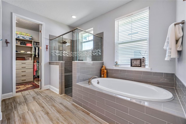bathroom featuring a walk in closet, a bath, a textured ceiling, a stall shower, and wood finished floors
