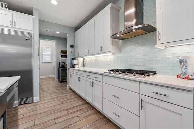 kitchen featuring white cabinetry, tasteful backsplash, wall chimney range hood, appliances with stainless steel finishes, and wood tiled floor