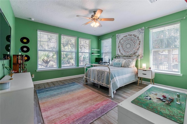 bedroom featuring baseboards, a textured ceiling, wood finished floors, and multiple windows