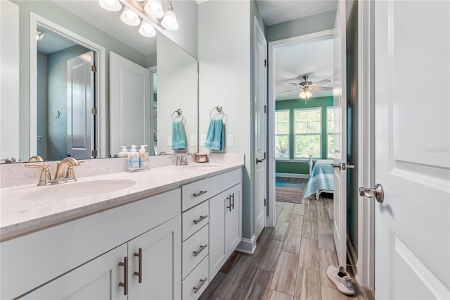 ensuite bathroom with baseboards, double vanity, a sink, and wood finished floors
