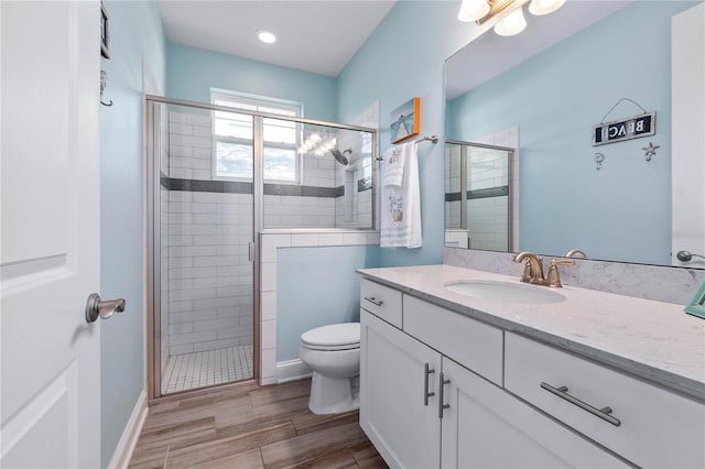 bathroom featuring vanity, toilet, baseboards, a stall shower, and wood finished floors