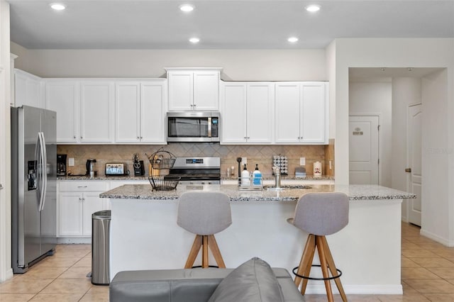 kitchen with a breakfast bar, stainless steel appliances, light tile patterned floors, and light stone counters